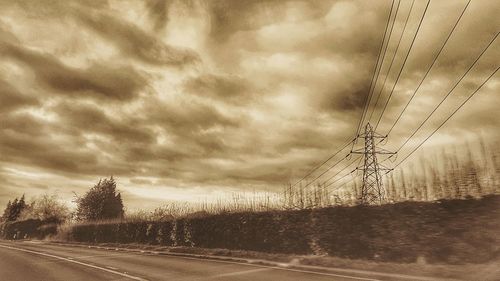 Road by electricity pylon against sky