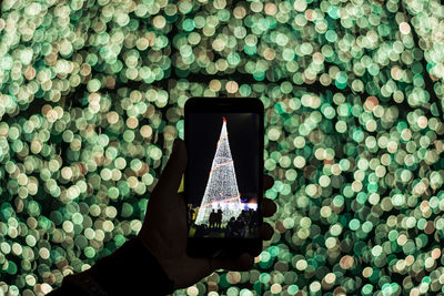 Close-up of hand holding mobile phone against illuminated decoration