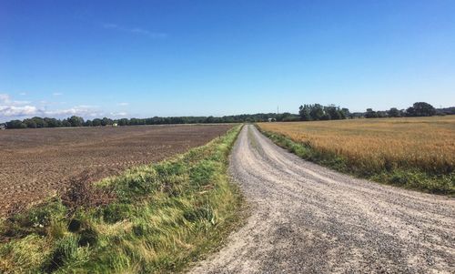 Dirt road passing through field against clear sky