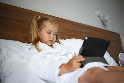 Cute girl using digital tablet sitting on bed at home