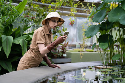 Side view of woman photographing while standing by plants 