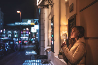 Woman drinking glass of illuminated building at night