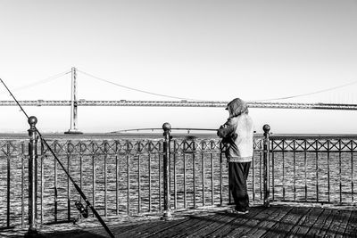 Rear view of person standing on promenade looking at bridge over river