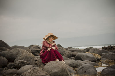 Rear view of person on rock at beach against sky