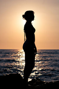 Silhouette woman standing at beach during sunset
