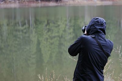 Rear view of man photographing by lake