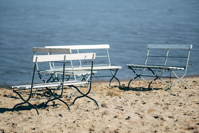 Empty benches on sand against sea at beach