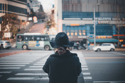 Rear view of woman in hat standing on city street