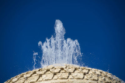 Low angle view of waves splashing on rocks against clear blue sky