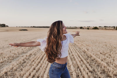 Carefree mid adult woman with arms outstretched standing on agricultural field