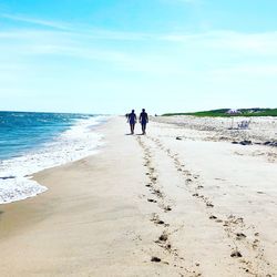 Rear view of couple walking at sandy beach during sunny day