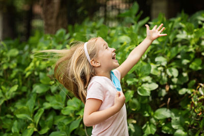 Side view of girl with mask standing against plants