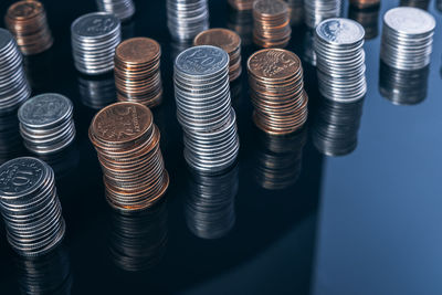 Piles of coins on a black, reflective surface seen from the top. inflation consuming our savings. 