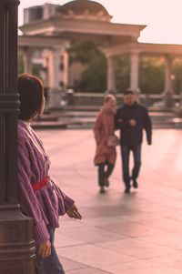 Rear view of a lone woman looking at a couple in city square