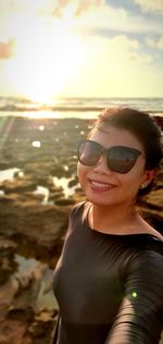 Portrait of young woman wearing sunglasses at beach during sunset