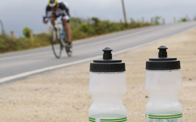 Man riding bicycle on road with water bottles in foreground