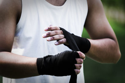 Midsection of boxer tying bandage while standing outdoors