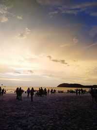 People walking on beach against sky during sunset
