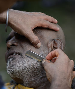 Cropped hands of barber shaving mature man beard