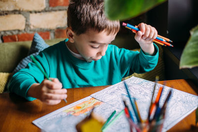 Portrait of a cute happy preschool boy at home or in a cafe draws.