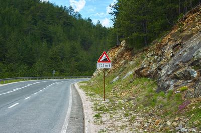 Road sign by trees against mountain