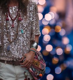 Midsection of woman holding bag while standing against illuminated lights