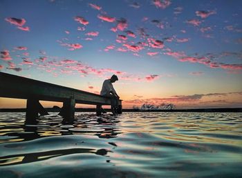 Man standing in sea against sky during sunset