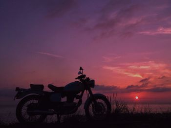 Silhouette bicycle on land against sky at sunset