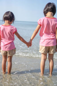 Rear view of sisters holding hands while standing at beach