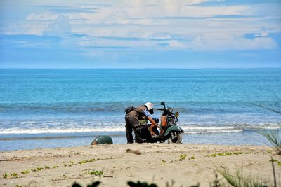 Man repairing scooter at beach against sky