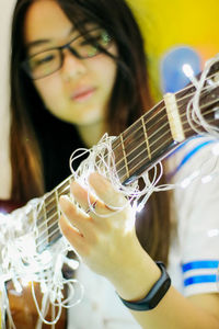 Young woman playing guitar with illuminated string lights at home