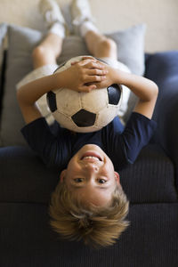 Portrait of boy with soccer ball lying on sofa at home
