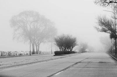 Empty road along bare trees against clear sky