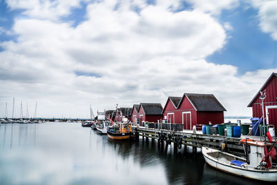 Boats moored by pier at harbor on lake against cloudy sky