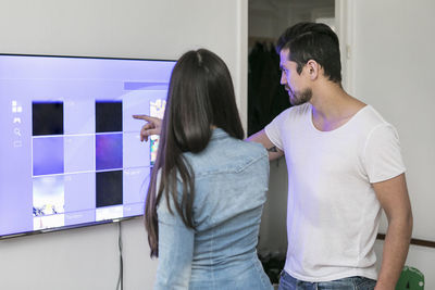 Young couple using touch screen television mounted on wall in living room