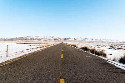 Road leading towards mountains against clear sky