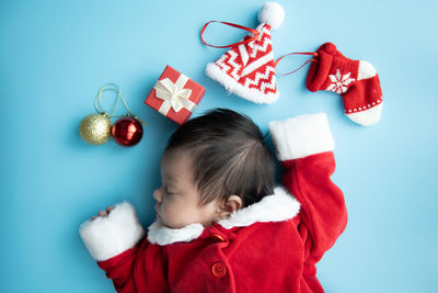 Directly above shot of baby girl wearing santa claus costume sleeping on blue background