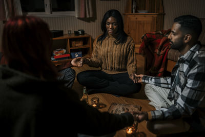 Multiracial friends holding hands sitting with ouija board in log cabin