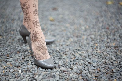 Low section of woman with tattoos wearing sandals while standing on ground