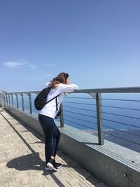 Full length of woman looking at view while standing by railing against blue sky during sunny day