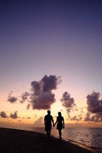 Silhouette couple walking at beach against sky during sunset