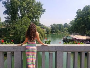 Rear view of woman standing by railing against lake