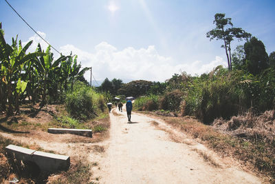 People walking on dirt road against sky