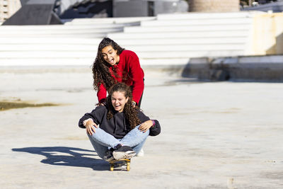 Playful female friends enjoying with skateboard outdoors