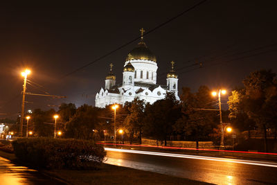 Illuminated street amidst buildings against sky at night