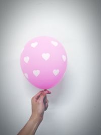 Close-up of hand holding pink balloons against white background