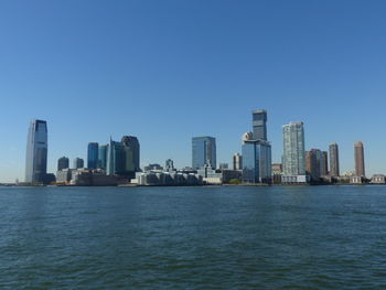Sea in front of cityscape against clear blue sky