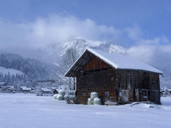 House on snow covered field by houses against sky