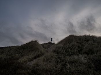 Low angle view of silhouette man standing on mountain against cloudy sky