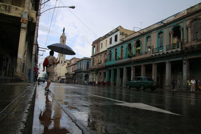 Man on wet street against sky in city